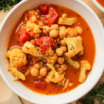 cauliflower chickpea curry in a white ceramic bowl on top of a wooden cutting board