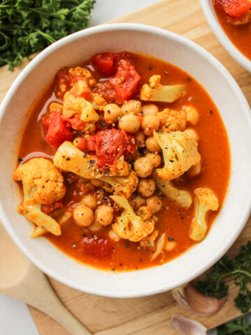 cauliflower chickpea curry in a white ceramic bowl on top of a wooden cutting board