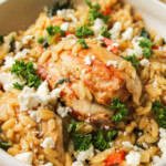 Mediterranean chicken orzo bake in a beige ceramic dish with feta and parsley on top