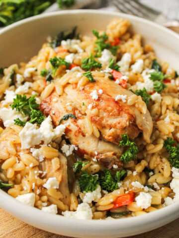 Mediterranean chicken orzo bake in a beige ceramic dish with feta and parsley on top