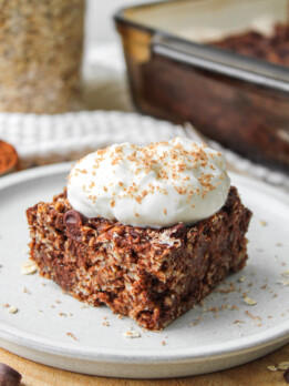 A square of double chocolate baked oatmeal topped with a dollop of Greek yogurt and chocolate shavings on top of a white ceramic plate
