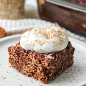 A square of double chocolate baked oatmeal topped with a dollop of Greek yogurt and chocolate shavings on top of a white ceramic plate