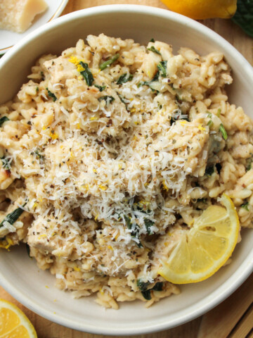 lemon chicken orzo pasta in a white ceramic dish topped with parmesan cheese and a slice of lemon