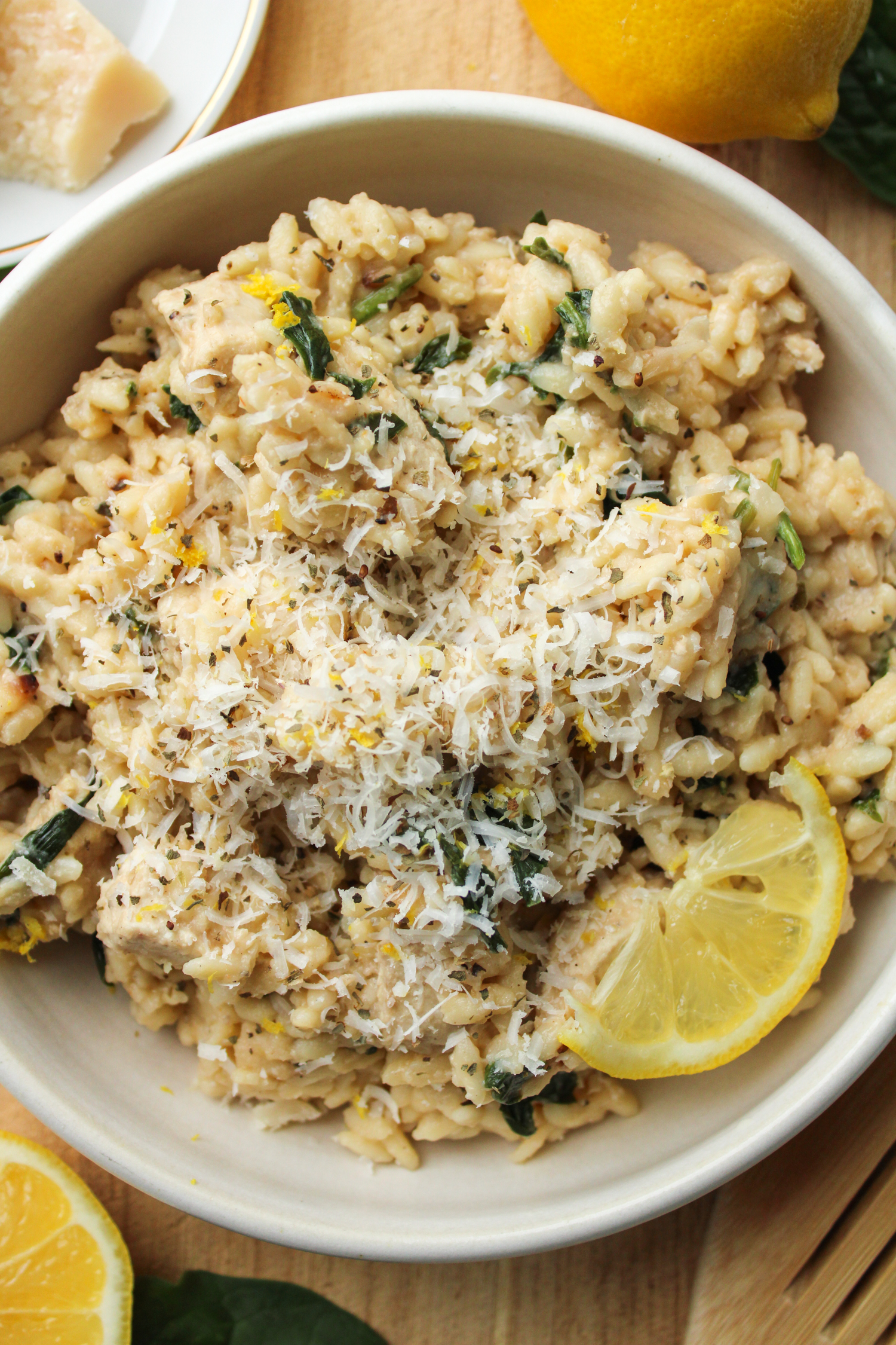 lemon chicken orzo pasta in a white ceramic dish topped with parmesan cheese and a slice of lemon