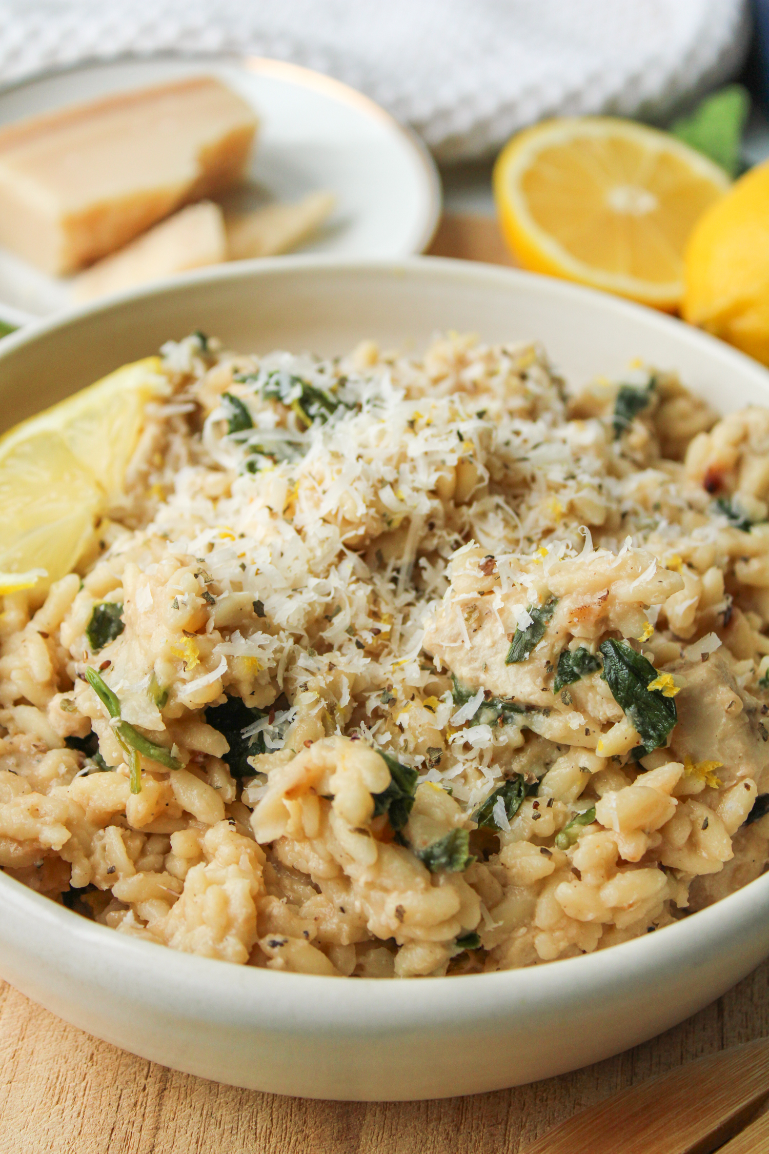 side shot of lemon chicken orzo pasta in a white ceramic dish topped with parmesan cheese and a slice of lemon