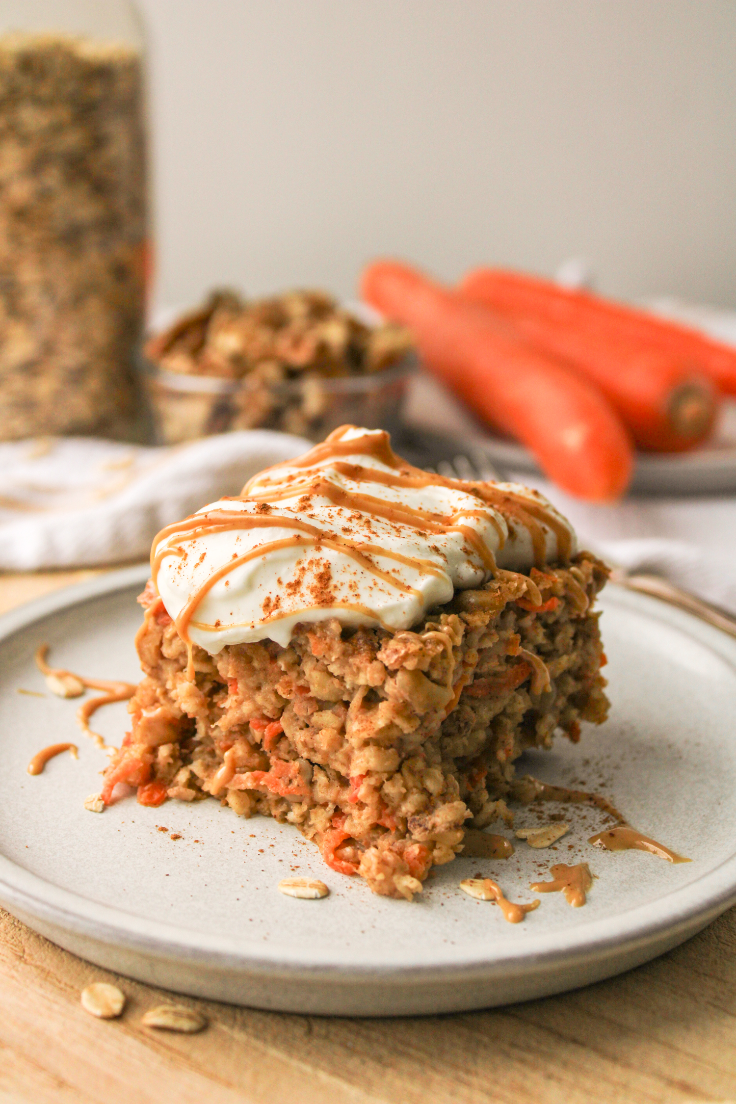 zoomed out of a slice of carrot cake baked oats on a grey ceramic plate topped with Greek yogurt and a drizzle of peanut butter