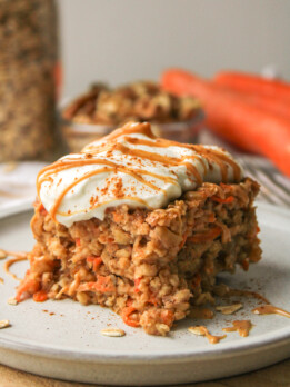 a slice of carrot cake baked oats on a grey ceramic plate topped with Greek yogurt and a drizzle of peanut butter