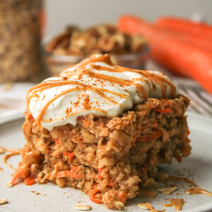 a slice of carrot cake baked oats on a grey ceramic plate topped with Greek yogurt and a drizzle of peanut butter