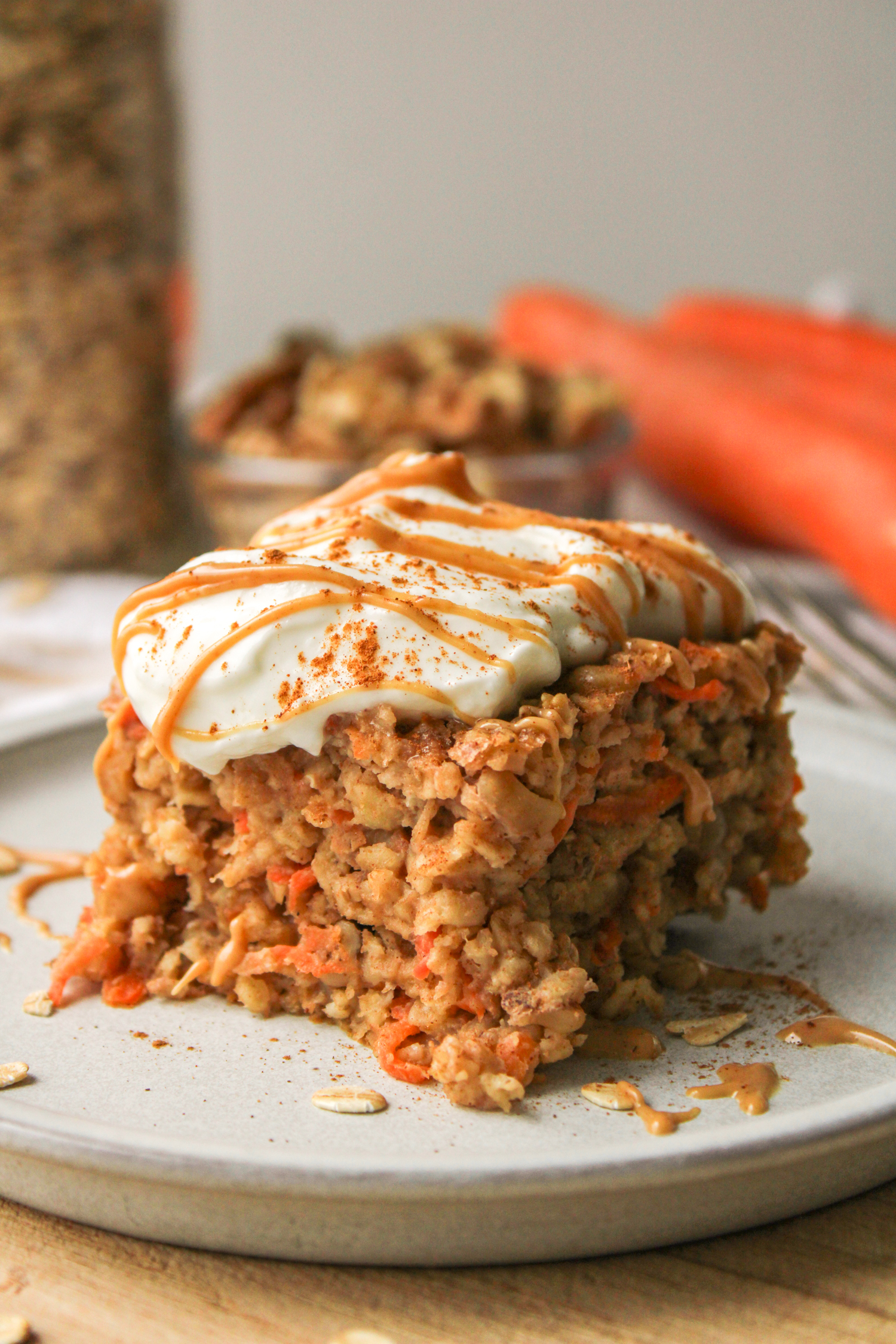 a slice of carrot cake baked oats on a grey ceramic plate topped with Greek yogurt and a drizzle of peanut butter