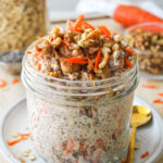 carrot cake overnight oats in a large glass mason jar topped with grated carrot, walnuts, cinnamon and peanut butter