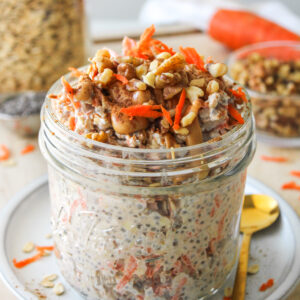 carrot cake overnight oats in a large glass mason jar topped with grated carrot, walnuts, cinnamon and peanut butter