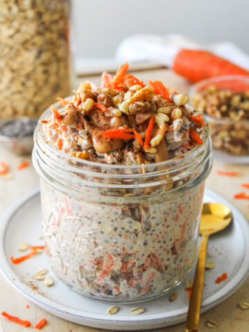 carrot cake overnight oats in a large glass mason jar topped with grated carrot, walnuts, cinnamon and peanut butter