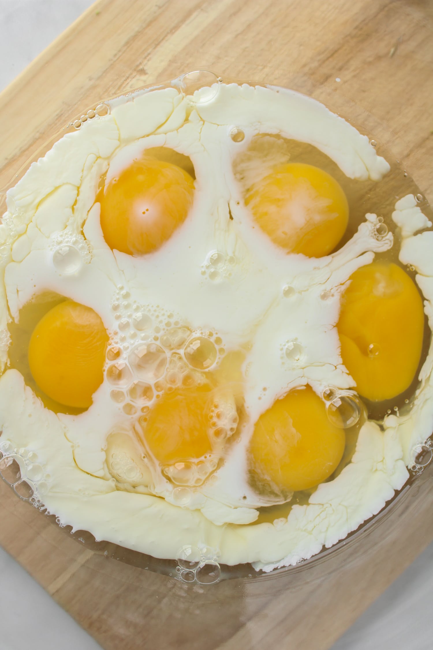 6 whole eggs and milk in a large glass bowl on top of a wooden cutting board