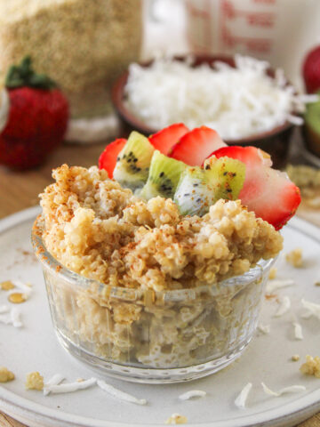 close up shot of quinoa coconut milk porridge in a small glass bowl topped with kiwi and strawberries