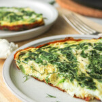 a slice of spinach and goat cheese frittata on a grey ceramic plate on top of a wooden cutting board