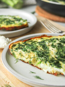 a slice of spinach and goat cheese frittata on a grey ceramic plate on top of a wooden cutting board