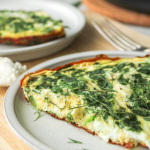 a slice of spinach and goat cheese frittata on a grey ceramic plate on top of a wooden cutting board