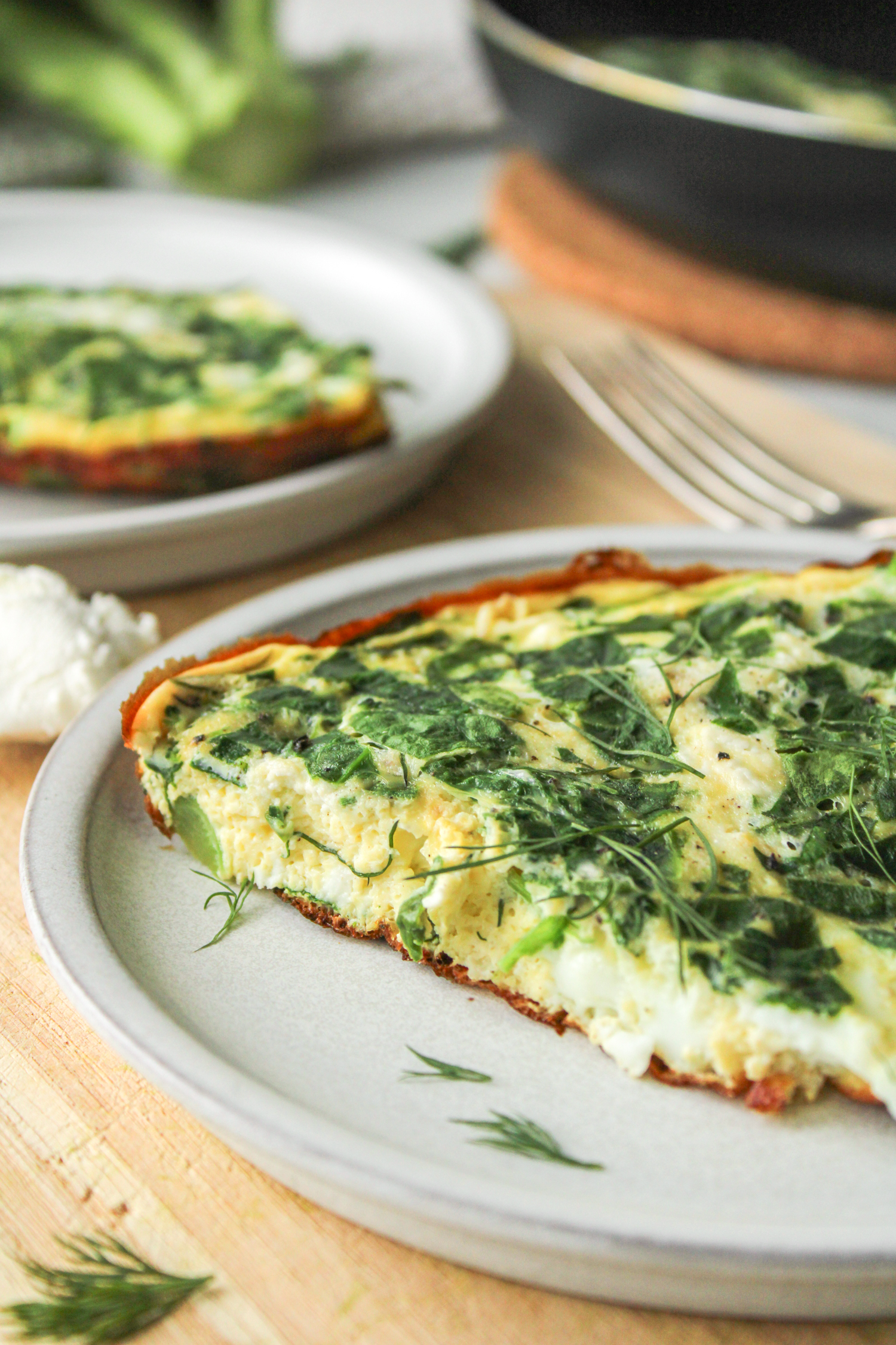 a slice of spinach and goat cheese frittata on a grey ceramic plate on top of a wooden cutting board