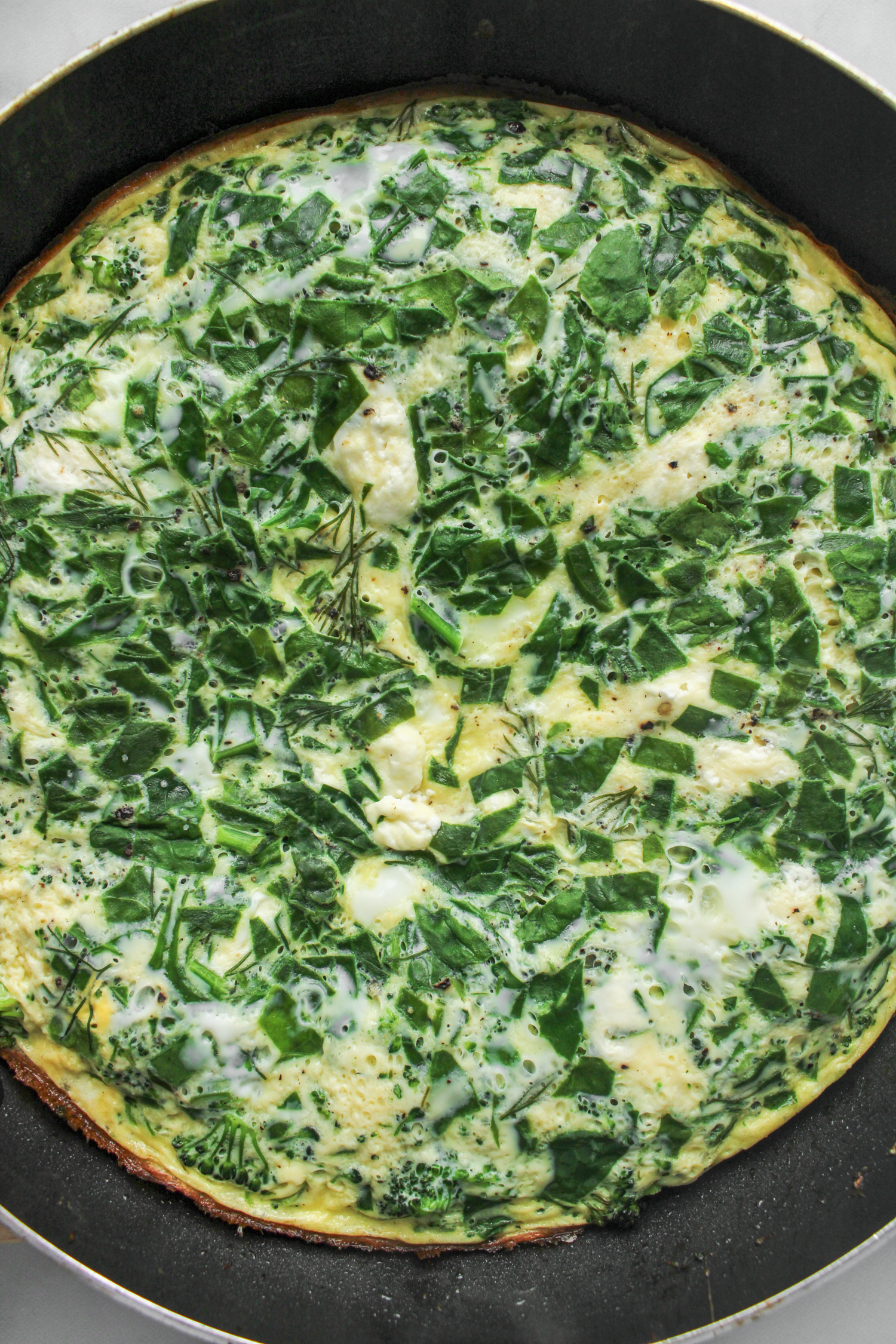 cooked spinach and goat cheese frittata in a large black frying pan