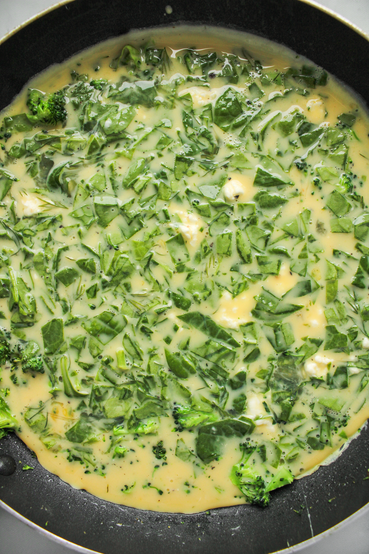 uncooked frittata in a large black frying pan