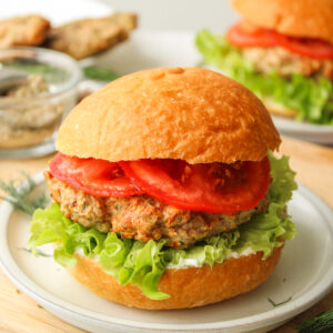 air fryer turkey burger with lettuce, tomato and tzatziki in a hamburger bun on a grey ceramic plate on top of a wooden cutting board