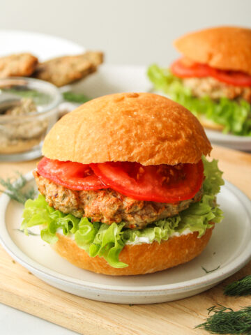 air fryer turkey burger with lettuce, tomato and tzatziki in a hamburger bun on a grey ceramic plate on top of a wooden cutting board