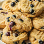 lemon blueberry cookies stacked on top of a white ceramic plate on top of a wooden cutting board