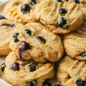 lemon blueberry cookies stacked on top of a white ceramic plate on top of a wooden cutting board