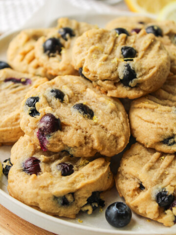 lemon blueberry cookies stacked on top of a white ceramic plate on top of a wooden cutting board
