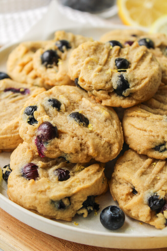 lemon blueberry cookies stacked on top of a white ceramic plate on top of a wooden cutting board