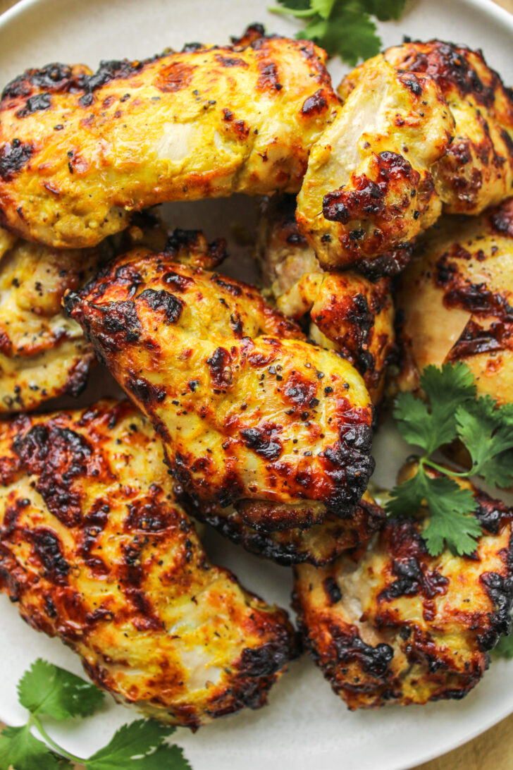 close up of air fryer curry chicken thighs on a white ceramic plate on top of a wooden cutting board