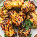 air fryer curry chicken thighs on a white ceramic plate on top of a wooden cutting board
