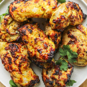 air fryer curry chicken thighs on a white ceramic plate on top of a wooden cutting board