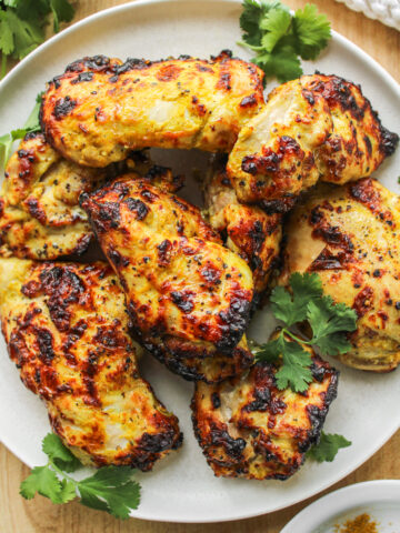 air fryer curry chicken thighs on a white ceramic plate on top of a wooden cutting board