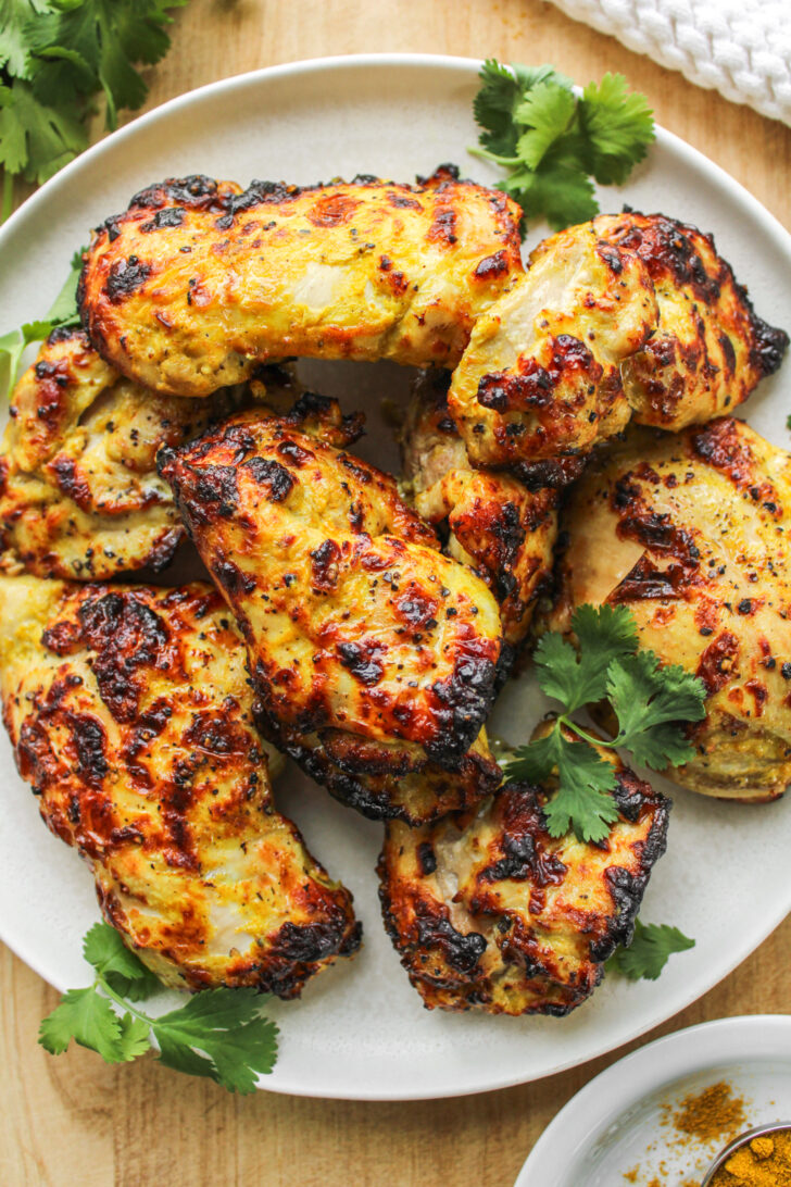 air fryer curry chicken thighs on a white ceramic plate on top of a wooden cutting board