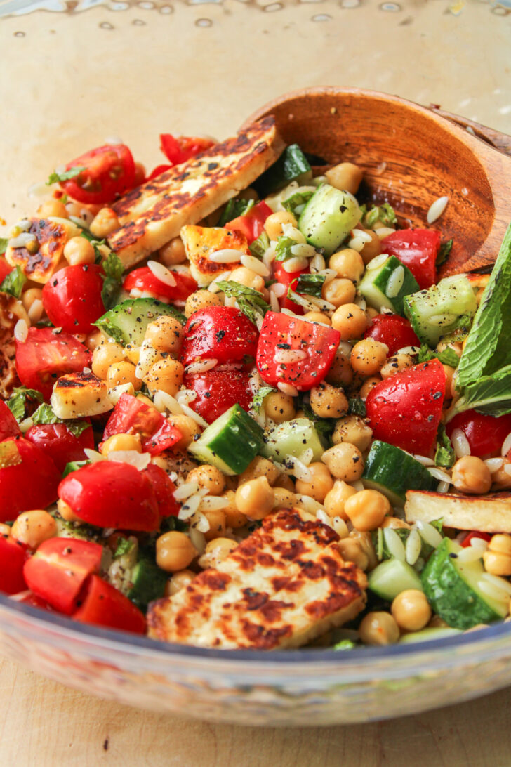 chickpea and halloumi salad with chili oil vinaigrette in a large bowl with wooden serving spoon