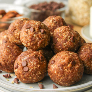 zoomed in shot of cookie dough protein balls stacked on top of each other on grey ceramic plates on top of a wooden board