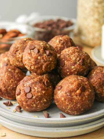 zoomed in shot of cookie dough protein balls stacked on top of each other on grey ceramic plates on top of a wooden board