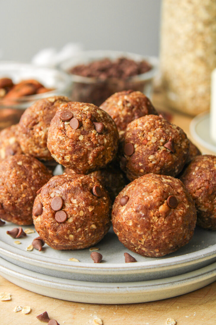 zoomed in shot of cookie dough protein balls stacked on top of each other on grey ceramic plates on top of a wooden board