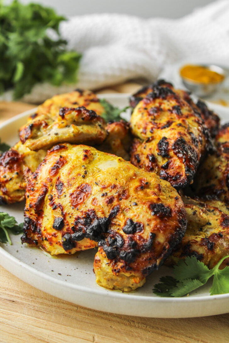 profile shot of air fryer curry chicken thighs on a white ceramic plate on top of a wooden cutting board