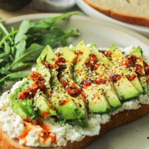 avocado ricotta cheese toast drizzled with chili oil on top of a ceramic plate