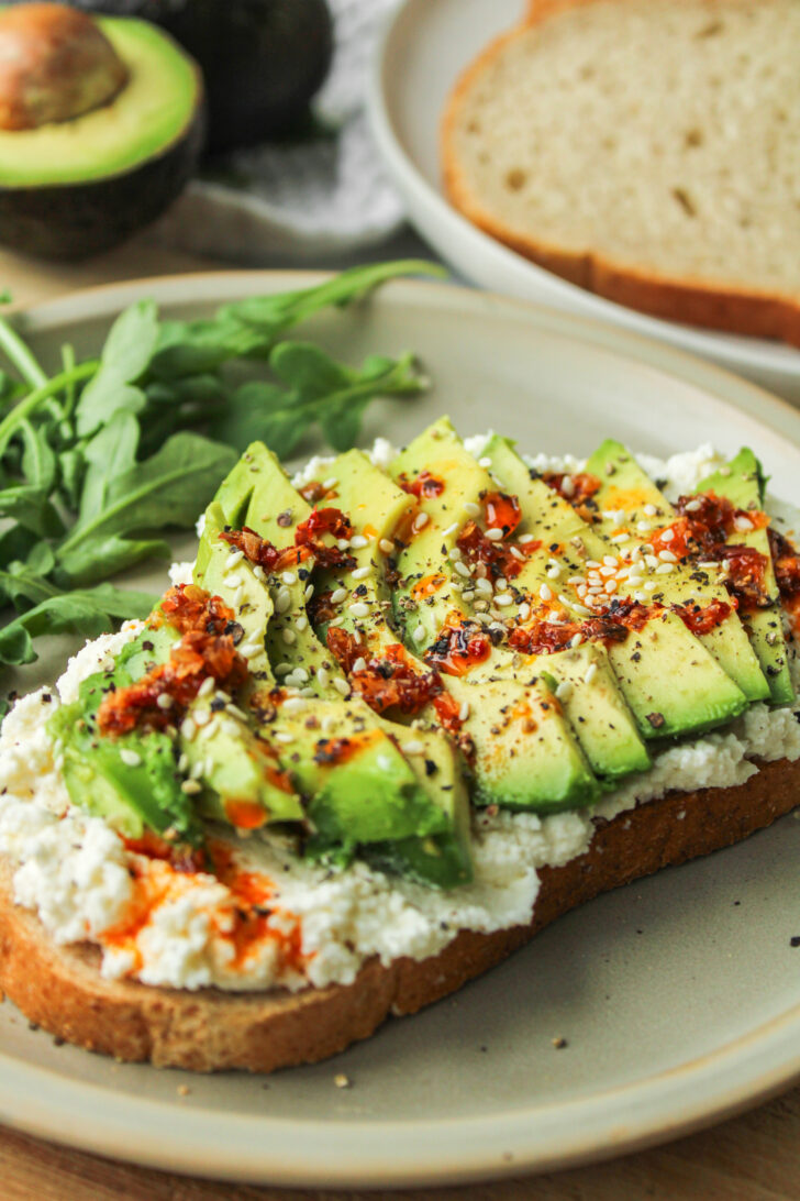 avocado ricotta cheese toast drizzled with chili oil on top of a ceramic plate