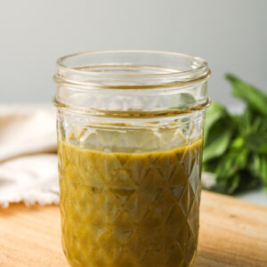 basil balsamic dressing in a small glass mason jar on a wooden cutting board