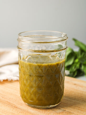 basil balsamic dressing in a small glass mason jar on a wooden cutting board