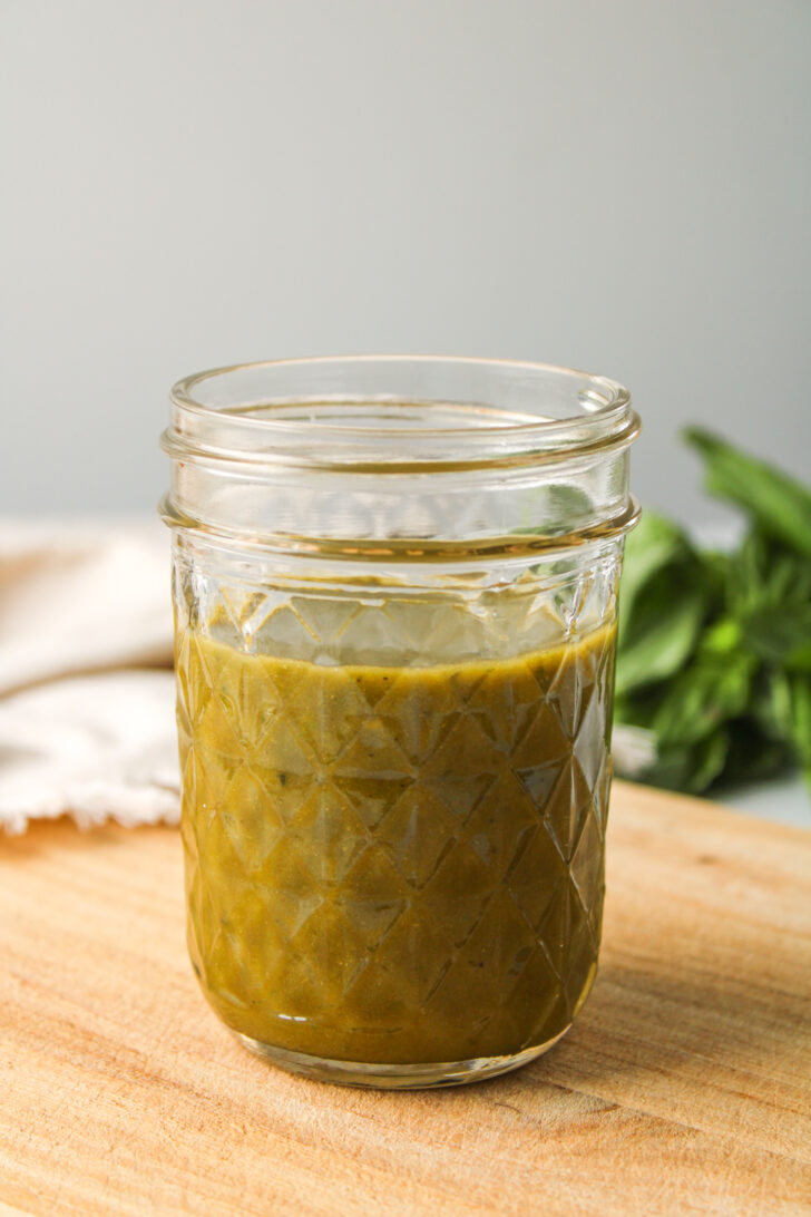 basil balsamic dressing in a small glass mason jar on a wooden cutting board