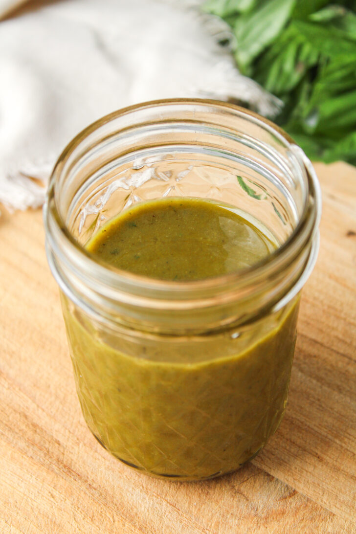 overhead shot of basil balsamic dressing in a small glass mason jar on a wooden cutting board