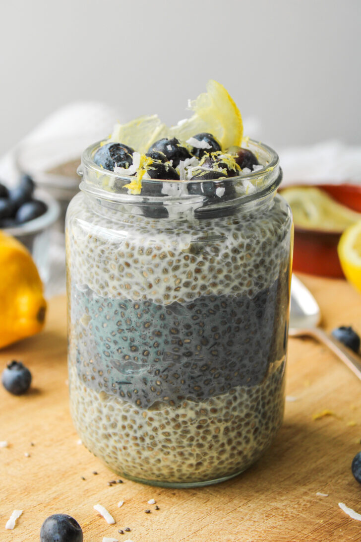 lemon blueberry chia pudding layered in a glass jar, topped with blueberries, lemon zest and coconut sitting on a wooden cutting board
