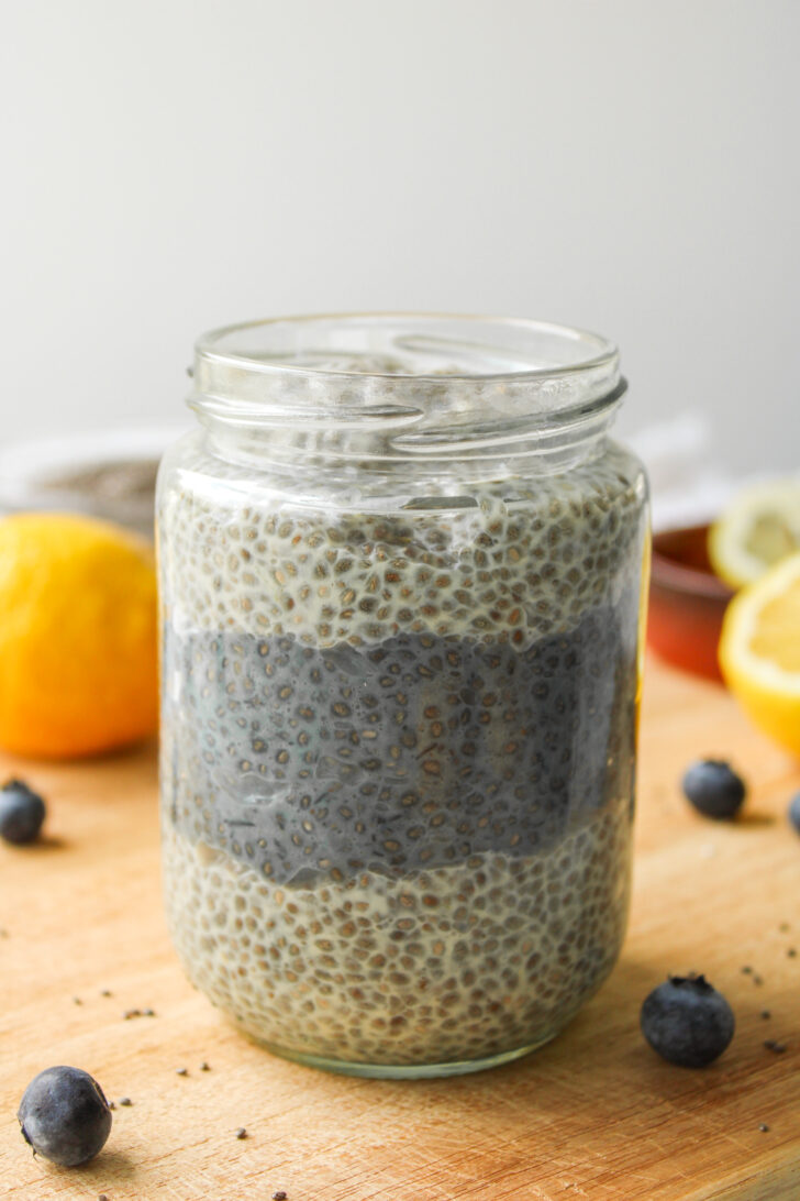 lemon blueberry chia seed pudding in a glass jar sitting on a wooden cutting board