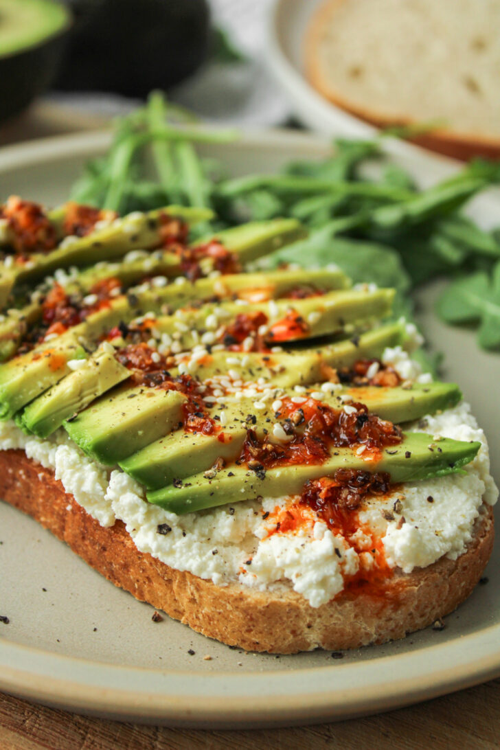 ricotta avocado toast drizzled with chili oil on top of a ceramic plate
