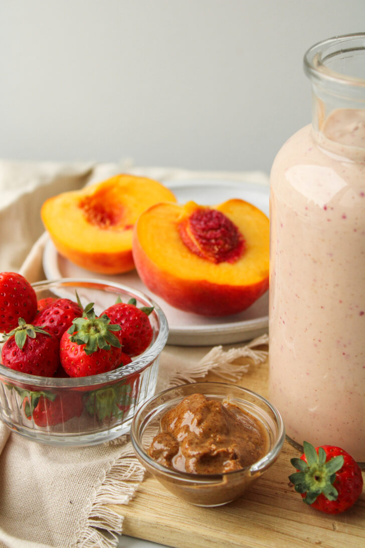 peach strawberry smoothie ingredients on a cutting board with smoothie off to the side